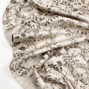 Peut inclure: Tissu beige avec un imprimé botanique de feuilles et de branches dans des tons bruns et gris. Le tissu est drapé, révélant les détails et la texture du motif. Idéal pour la décoration intérieure ou les projets de couture.