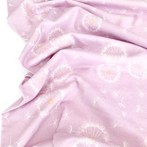 May include: A light purple fabric with a repeating pattern of white dandelion seed heads and stems. The fabric is gathered and folded, showing the texture and design. The dandelion heads have a light orange center.