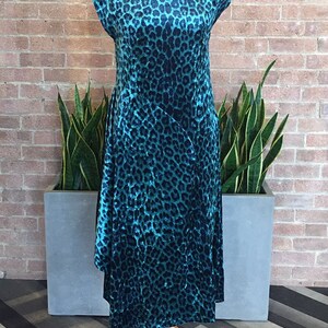 May include: A teal blue dress with a black leopard print pattern. The dress has a scoop neck and short sleeves. It is displayed on a mannequin against a brick wall.