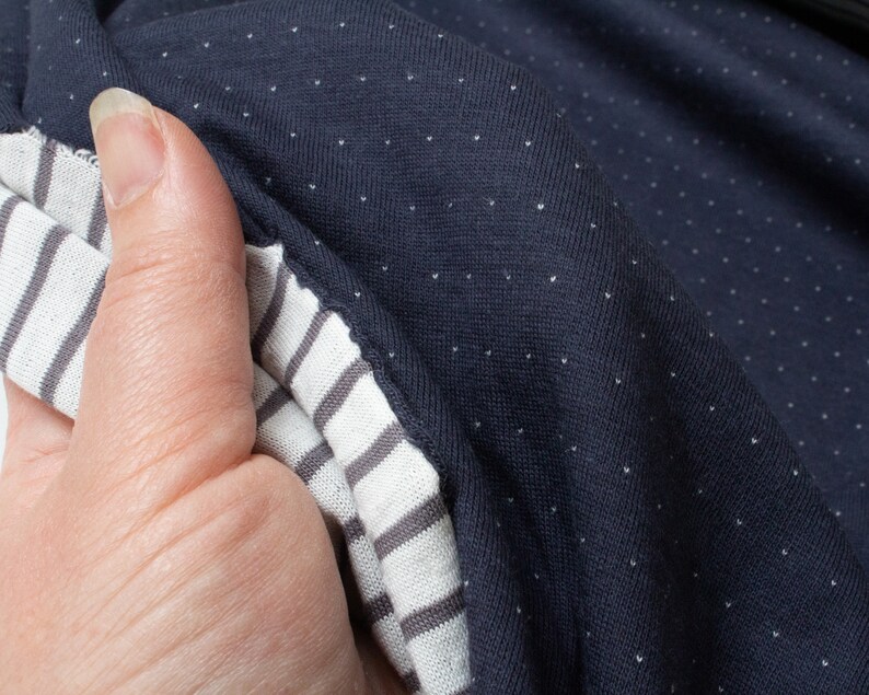 May include: Close-up of a navy blue fabric with white polka dots. The fabric is folded over a white and gray striped fabric.