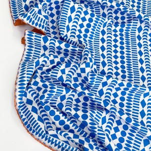 Könnte beinhalten: Weißer Stoff mit einem blauen geometrischen Muster. Das Muster enthält Kreise, Rauten und Halbmonde.