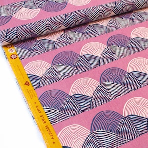 Puede incluir: Tela rosa con un patrón repetido de arcos rayados blancos y azul marino. La tela tiene un borde blanco con el texto "Ruby Star Society" y "Collection: Delicious" impreso en amarillo.