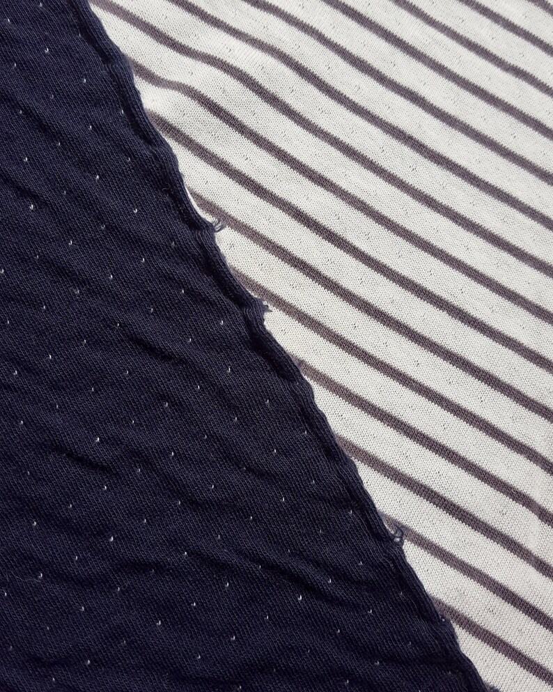 May include: Close-up of two different fabrics sewn together. One side is a dark blue fabric with a subtle dotted pattern. The other side is a white fabric with thin, gray stripes.