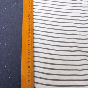 May include: A wooden ruler with inch markings is placed next to two fabric swatches. The fabric on the left is a dark blue with white polka dots. The fabric on the right is white with thin gray stripes.