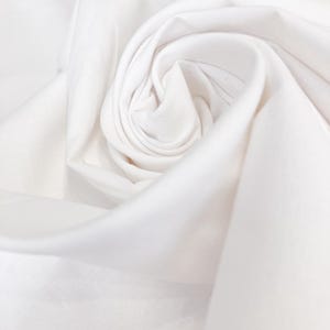 May include: Close-up of a tightly swirled, pristine white fabric. The fabric is soft and appears to be made of a lightweight material, with visible folds and textures. The overall impression is one of purity and simplicity.