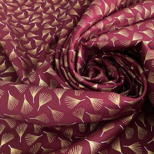 May include: Burgundy fabric with a repeating pattern of gold stylised leaves. The fabric is folded and draped.