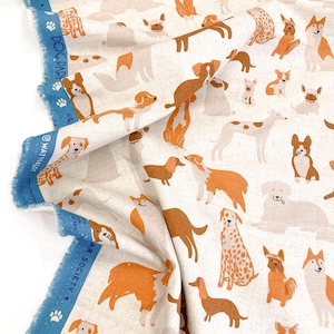 May include: A white fabric with a repeating pattern of brown, orange, and white dogs. The fabric has a blue border with the text "Dog Park Society" and paw prints.