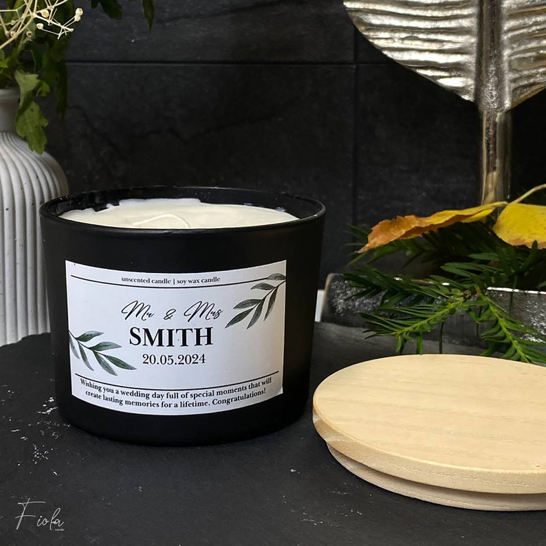 May include: Black soy wax candle with a white label that says "unscented candle | soy wax candle", "Mr & Mrs SMITH", "20.05.2024", and "Wishing you a wedding day full of special moments that will create lasting memories for a lifetime. Congratulations!" The candle has a wooden lid.