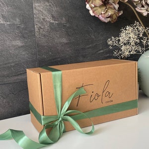 May include: A brown cardboard box with a green satin ribbon tied around it. The box has the text "Fioia candle" printed on the top.