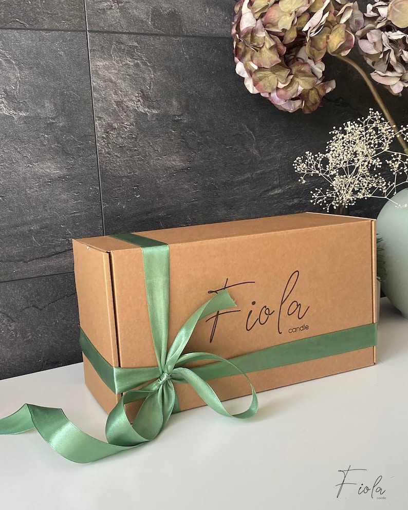 May include: A brown cardboard box with a green satin ribbon tied around it. The box has the text "Fioia candle" printed on the top.