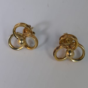 May include: A pair of gold-toned earrings with a clover-like design. Each earring features three interlocking circles with a small ball in the center.