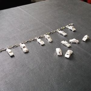 May include: A silver charm bracelet with a variety of car charms, including a classic car, a sports car, and a truck. The charms are attached to a silver chain.
