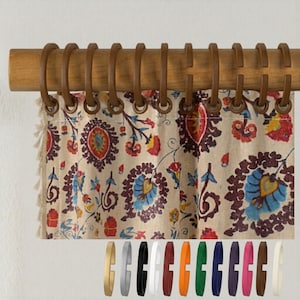 May include: Wooden curtain rod with brown rings and a patterned curtain. The curtain has a beige background with a floral design in red, blue, and yellow. The rod is mounted on a white wall.