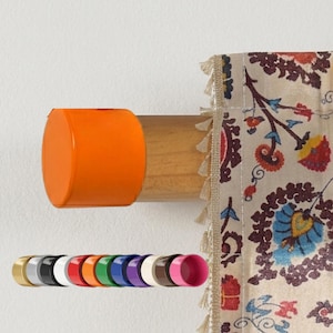 May include: A wooden curtain pole with an orange end cap is mounted on a white wall. A patterned curtain with floral designs hangs to the right. Several colour options for the end cap are shown below.