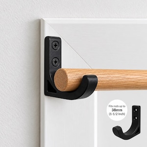 May include: A matte black metal wall bracket holding a light-colored wooden rod. The bracket is secured with two screws and features a curved cradle design. Text on the image states: Fits rods up to 38mm (1-1/2 Inch).