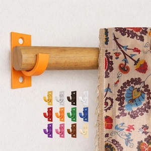 May include: A wooden curtain rod with an orange bracket and hook, paired with a patterned curtain. Below, a selection of colorful hooks in yellow, white, brown, green, blue, purple, pink, and beige are displayed.