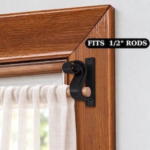 Puede incluir: Un soporte de metal negro para barra de cortina con diseño de voluta montado en un marco de ventana de madera. El soporte sostiene una barra de madera clara con una cortina blanca traslúcida. El texto FITS 1/2" RODS es visible a la derecha.