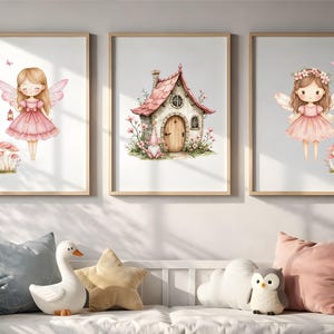 May include: Three framed wall art prints featuring watercolour illustrations. The left and right prints show a fairy in a pink dress with wings, while the centre print depicts a small cottage with a pink roof, surrounded by flowers and mushrooms.