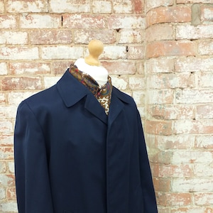 Puede incluir: Un abrigo largo azul marino con cierre de un solo botón y cuello. El abrigo está en un maniquí que lleva una bufanda estampada.