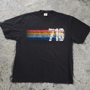 May include: A black short-sleeve t-shirt featuring a distressed graphic design across the chest. The graphic consists of three horizontal stripes in red, yellow, and blue, overlaid with the white distressed text 716.