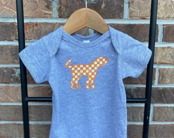 May include: A gray short-sleeved baby onesie with an orange and white checkered dog silhouette.