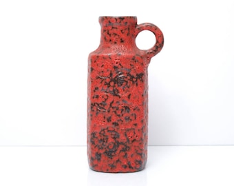 May include: A red ceramic vase with a textured surface and a black handle. The vase has a unique, abstract design.
