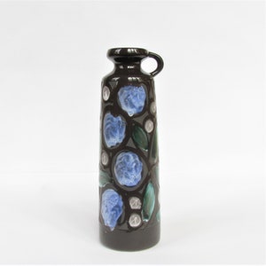 Peut inclure: Un vase en céramique brun avec un motif floral bleu et vert. Le vase a une petite poignée sur le côté.