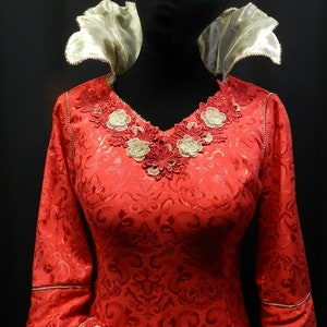 May include: A red dress with a gold lace neckline and a white collar. The dress has a floral pattern and long sleeves.