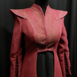 May include: A long, red, sparkly jacket with a high collar and a black skirt underneath. The jacket has a split in the back and black lace trim on the sleeves.