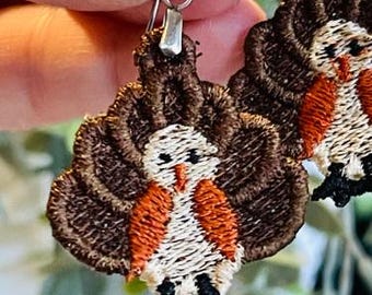 May include: A pair of brown, orange, and white embroidered bird earrings with silver hooks.