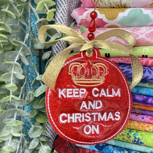May include: Red glitter Christmas bauble with a gold ribbon and a gold crown. The bauble says "Keep Calm and Christmas On".