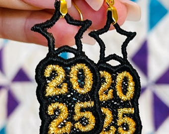 Può includere: Orecchini a forma di stella dorati con tessuto nero e ricamo dorato dei numeri 2025.