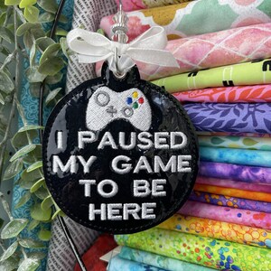 May include: A black and white round ornament with a white video game controller and the text "I paused my game to be here".