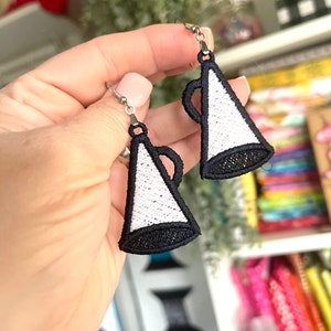 May include: A pair of silver earrings with white and black embroidered megaphone designs.