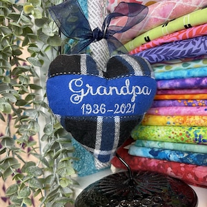 以下が含まれることがあります： 青いリボンに「Grandpa 1936-2021」と刺繍された、青と黒の格子柄のハート型のオーナメントです。