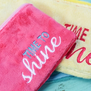 May include: Two fuzzy zippered pouches with the text "Time to Shine" on the pink pouch and "Time to Shine" on the yellow pouch.