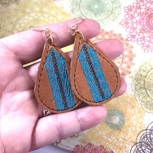 May include: A pair of teardrop-shaped leather earrings with a blue and brown striped design. The earrings have gold hooks.