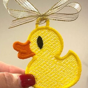 May include: A yellow embroidered rubber ducky ornament with a gold ribbon. The ducky has a black eye and an orange beak.