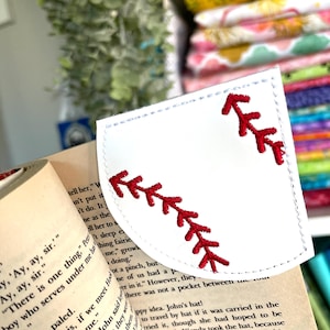 May include: White fabric bookmark with a red baseball stitch design. The bookmark is shaped like a baseball glove with the stitching on the outside of the glove.