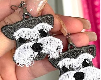 Pode incluir: Um par de brincos de prata com um design de schnauzer bordado em branco e cinza.