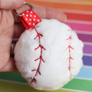 May include: White plush baseball keychain with red stitching and a red and white polka dot ribbon.