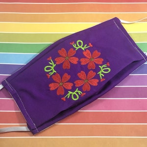 May include: Purple face mask with a floral embroidery design featuring five red flowers with green stems and leaves.