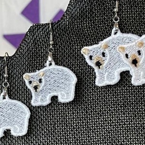 May include: A pair of white polar bear dangle earrings with silver hooks. The bears are embroidered with white thread and have brown eyes.