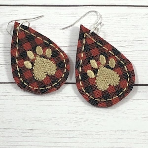May include: A pair of red and black plaid teardrop-shaped earrings with gold paw print embroidery.