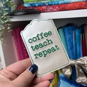 May include: White fabric tag with green embroidered text that reads "coffee teach repeat".