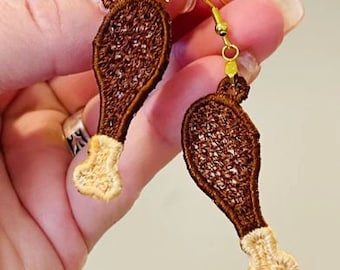 May include: A pair of gold dangle earrings featuring a brown and beige embroidered design of a chicken leg.