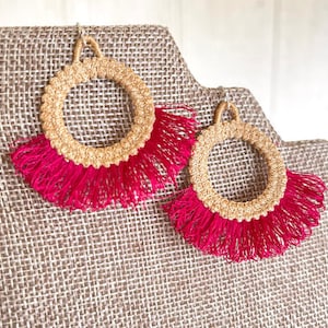 Puede incluir: Un par de pendientes de borla dorados y rosados. Los pendientes están hechos de un material tejido y tienen una franja de borlas rosadas.
