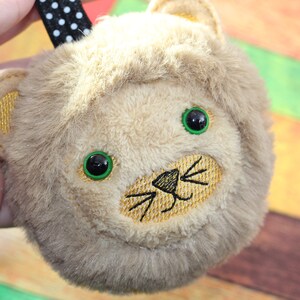 May include: A plush lion head with a brown and white fur texture. The lion has green eyes and a gold embroidered nose and whiskers.