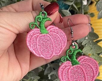 May include: Pink embroidered pumpkin earrings with green stems. The earrings are a festive accessory, perfect for autumn or Halloween. The pumpkin design is detailed with a textured, stitched appearance, and the earrings have a silver-colored hook.