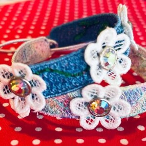 May include: Two denim bracelets with white lace flowers and clear rhinestone centers. The bracelets are on a red background with white polka dots.